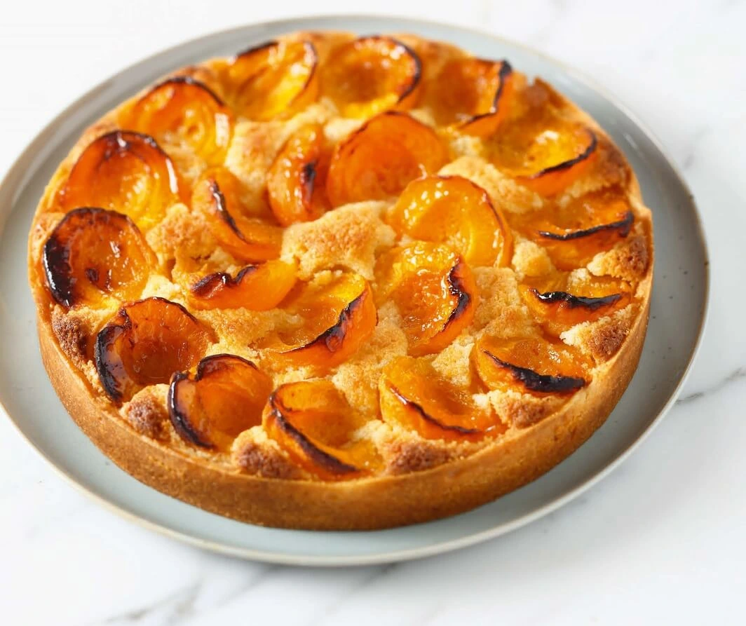 Golden apricot tart with almond cream in a crisp pâte sucrée shell, arranged in a rosette pattern and finished with a glossy glaze